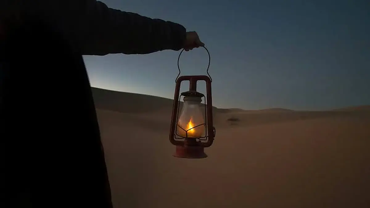 Mano sosteniendo un farol rojo encendido al atardecer en las dunas del Sáhara, Ramadán en Marruecos 2027